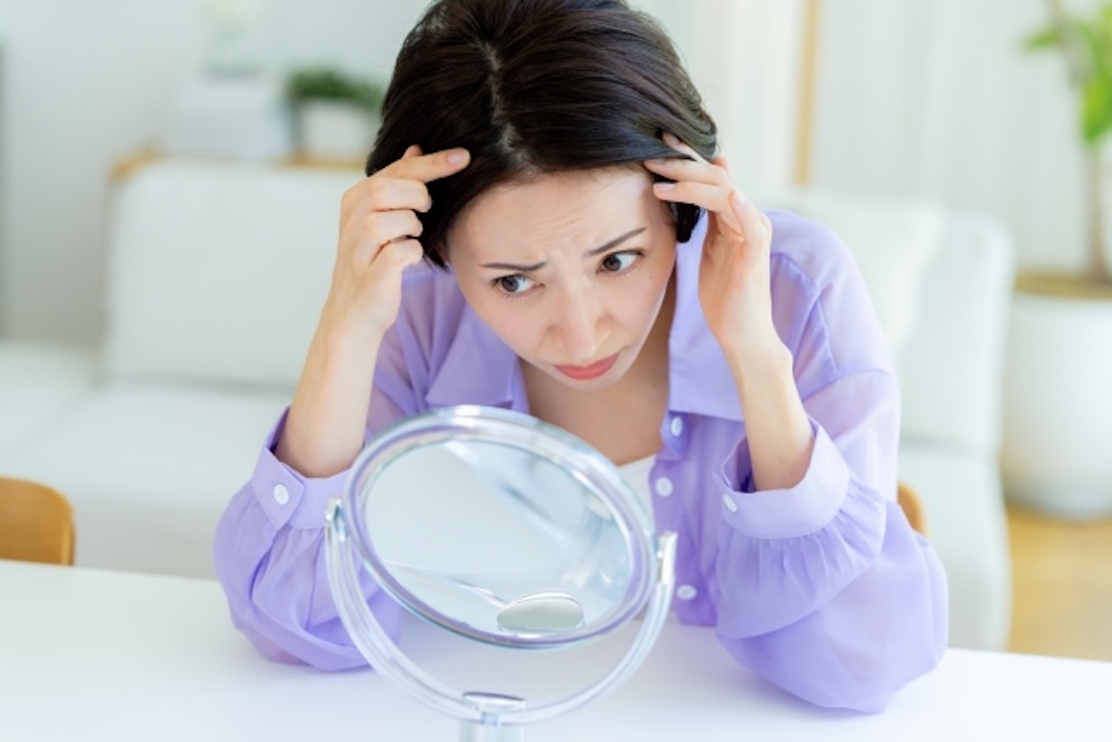 鏡を見て生え際を気にする女性