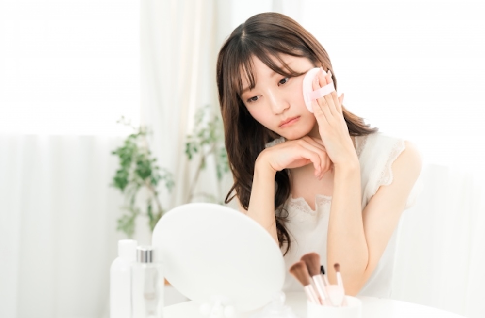 鏡を見て肌荒れを気にする女性